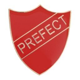 Red enamel prefect badge featuring gold raised lettering on traditional shield shape with secure metal pin back for school uniform attachment